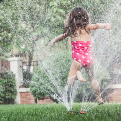 Little girl jumping through a sprinkle as father watched,